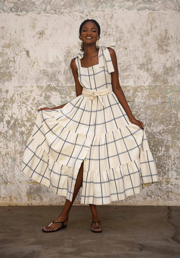 Woman wearing imara dress with blue plaid pattern against a textured wall.